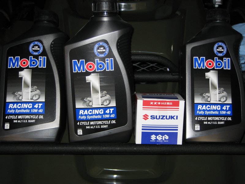 Three Mobil 1 Racing 4T 10W-40 oil quarts and a boxed Suzuki oil filter on a shelf