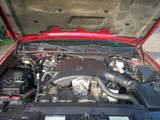 2000 Ford Crown Victoria - The engine compartment of a red vehicle is displayed with the hood raised, revealing the engine and surrounding parts.