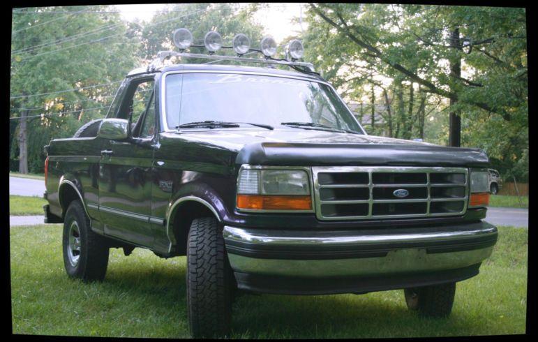 Black Ford Bronco with top off and five-lamp windshield light bar parked on grass