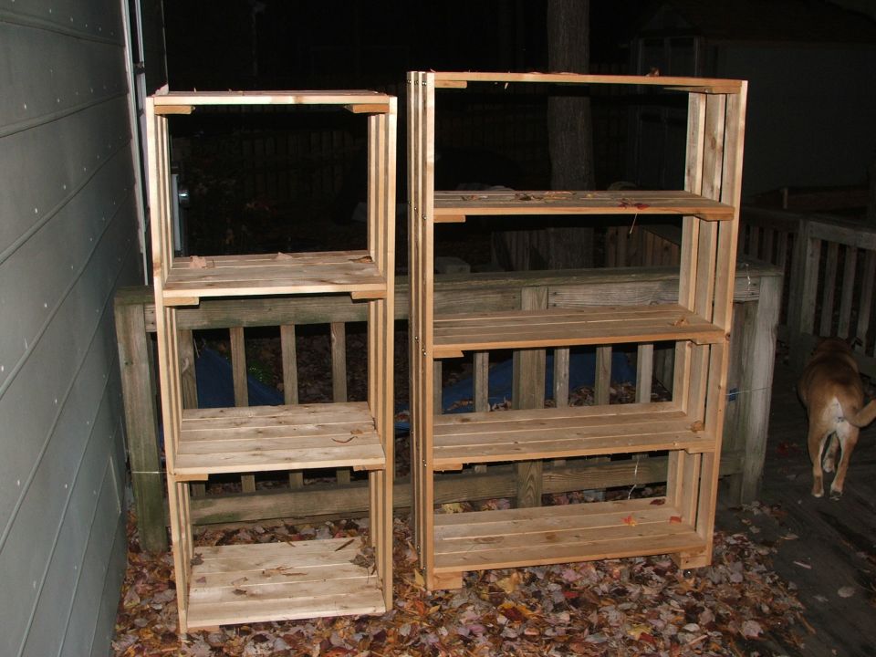 Two unfinished wooden shelving units on a deck with a dog walking away