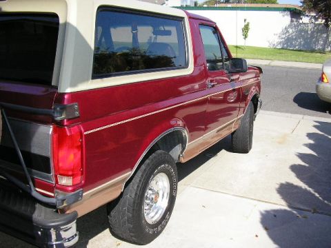 1994 Ford Bronco - The side profile of a red Ford Bronco with a tan removable top is shown parked on a driveway.