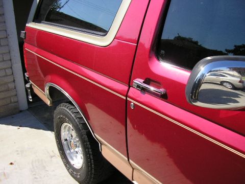 1994 Ford Bronco - Side profile of a red Ford Bronco, highlighting its body lines and tan accents.