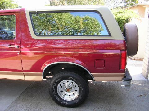 1994 Ford Bronco - The side profile of a red SUV shows its two-tone paint scheme and a rear-mounted spare tire.