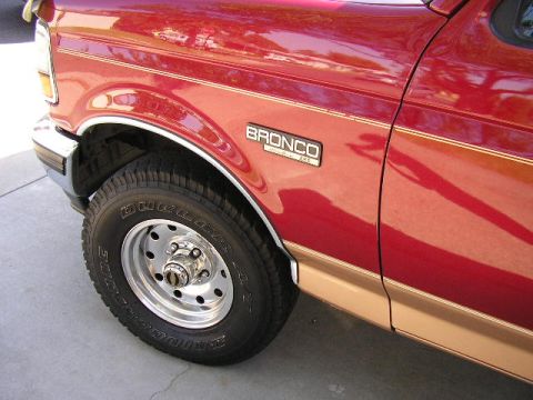 1994 Ford Bronco - Close-up of a red 1994 Ford Bronco's front fender and wheel, showing the 'BRONCO' badge and two-tone paint.