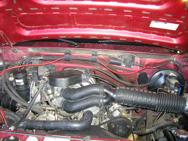 Engine bay with red hood, hoses, and engine components visible. Watermark says SUPERMOTORS.NET