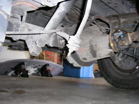 1994 Ford Bronco - Undercarriage view of rear axle and suspension parts, with a surfboard and boots nearby.