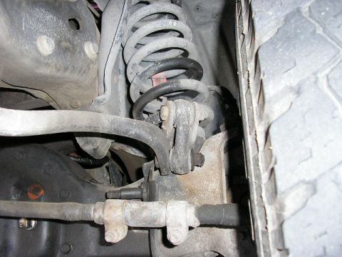 1994 Ford Bronco - This image shows a close-up view of a vehicle's suspension system, including a coil spring and various linkage components.
