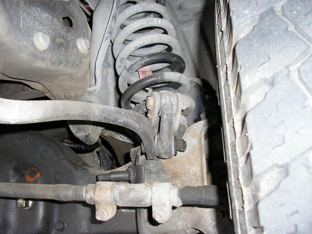 Close-up of a vehicle's front suspension with a coil spring, control arm, and tie rod visible