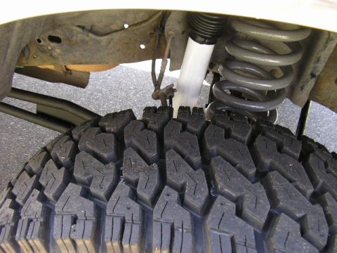1994 Ford Bronco - A close look up into the front wheel well showing a white-bodied shock absorber with black rubber boot alongside a gray-painted coil spring…