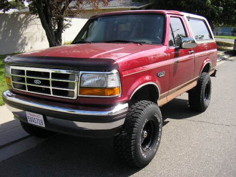 1994 Ford Bronco - Front three-quarter view of a lifted full-size Ford Bronco in dark red with tan lower two-tone body cladding and a tan hardtop, wearing whi…