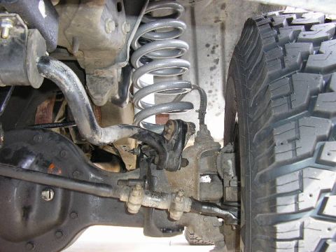 1994 Ford Bronco - Underside view of a 4x4 front suspension showing a coil spring, sway bar, steering linkage with adjusting sleeves, brake hose, and the fron…