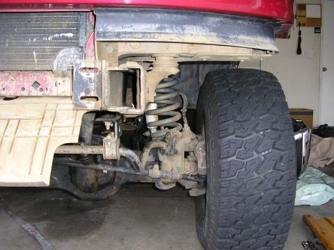1994 Ford Bronco - Close-up of the front suspension and tire assembly on a red 1994 Ford Bronco during a tow hook installation.