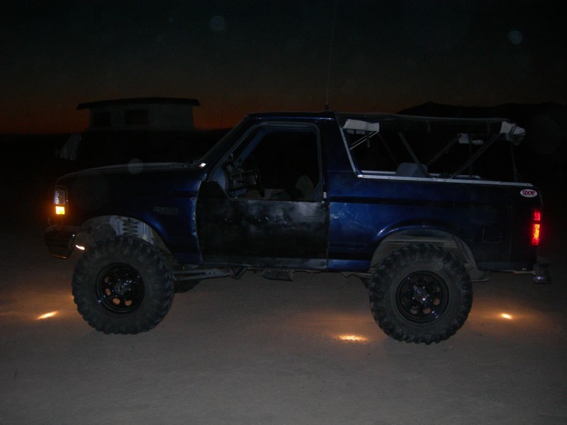 Blue 1994 Ford Bronco side view with off-road tires at night