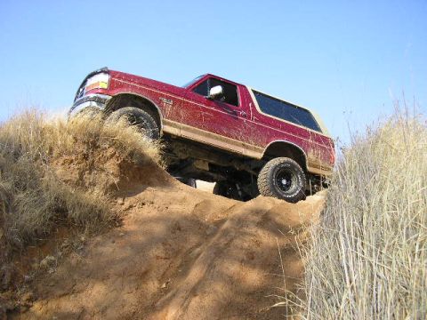 1994 Ford Bronco - A red Ford Bronco navigates a steep dirt incline under a bright blue sky.