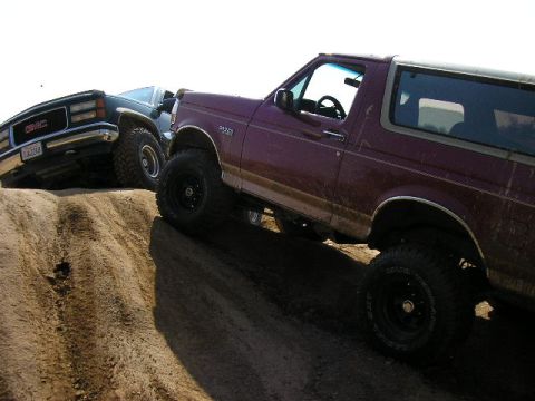 1994 Ford Bronco - A maroon 1994 Ford Bronco and a dark GMC truck navigate a steep dirt incline.