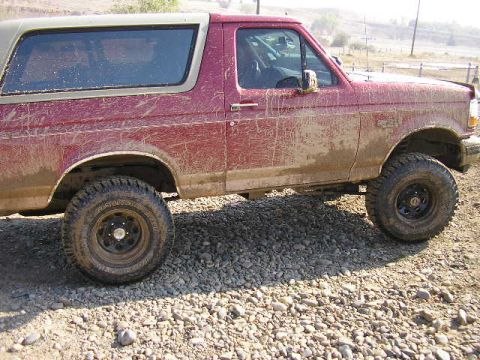 1994 Ford Bronco - Mud-covered 1994 Ford Bronco parked on a gravelly surface.