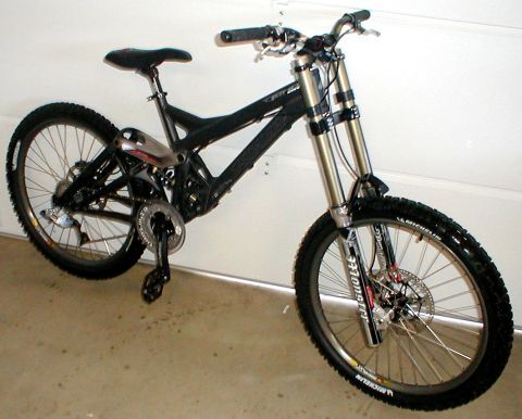 1996 Ford Bronco - A black full-suspension downhill mountain bike photographed from the drive side against a white garage wall, standing on a concrete floor.…
