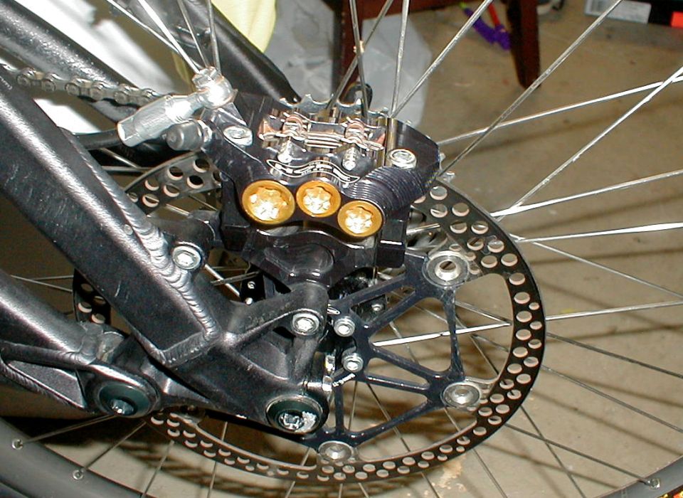 Rear bicycle disc brake caliper with three gold pistons and drilled rotor