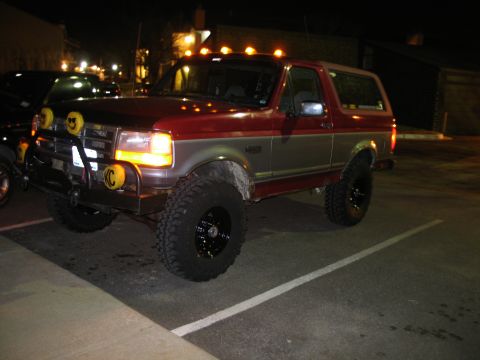 1995 Ford Bronco - A lifted two-tone red and tan 1990s Ford Bronco full-size SUV photographed at night in a parking lot, shown from the front three-quarter an…