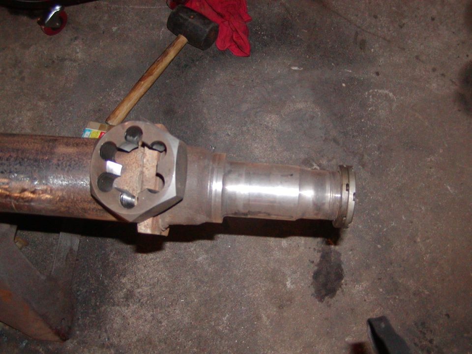 Differential axle housing with a large hex nut tool attached, a sledgehammer rests nearby