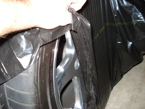 1998 Ford Taurus - A person is holding black plastic sheeting over a tire and wheel assembly.