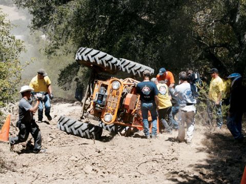 1973 Ford Bronco - An off-road vehicle has overturned on a dirt track, with several people observing the scene.