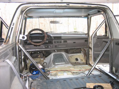1996 Ford Bronco - The interior of a 1996 Ford Bronco shows a custom roll cage and a stripped-down dashboard.