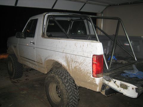 1996 Ford Bronco - Mud-covered 1996 Ford Bronco with a roll cage, parked indoors.