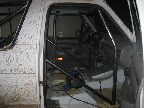 1996 Ford Bronco - The interior of a white off-road vehicle shows extensive roll cage modifications and mud-splattered exterior panels.