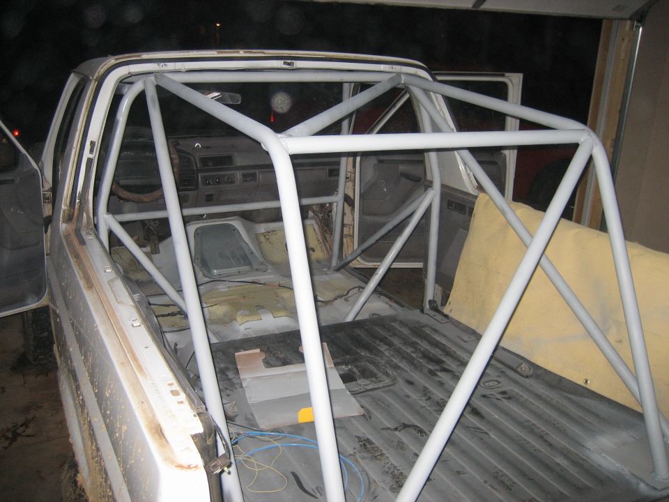 Gray-primered roll cage in a roofless stripped Ford truck cab and bed at night