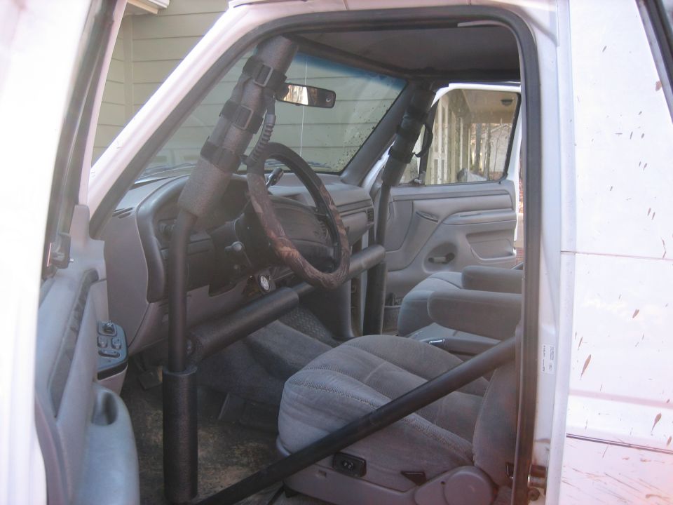 Grey Ford truck interior with black roll cage seen through the open driver door