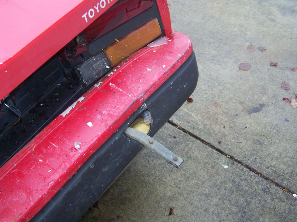 Red Toyota car rear bumper with black trim, showing damage and a metal bracket protruding
