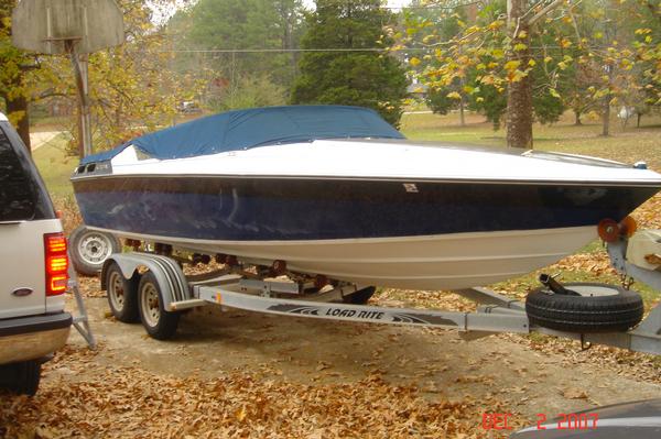 Blue and white covered speedboat on a tandem-axle trailer in a leaf-covered driveway