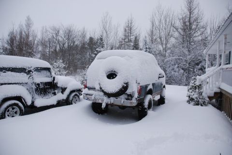 1996 Ford Bronco - Two SUVs are buried in snow during a winter storm, with a house visible in the background.