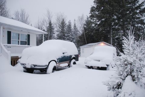 1996 Ford Bronco - Two vehicles are buried in snow during a winter storm, parked in a residential driveway.