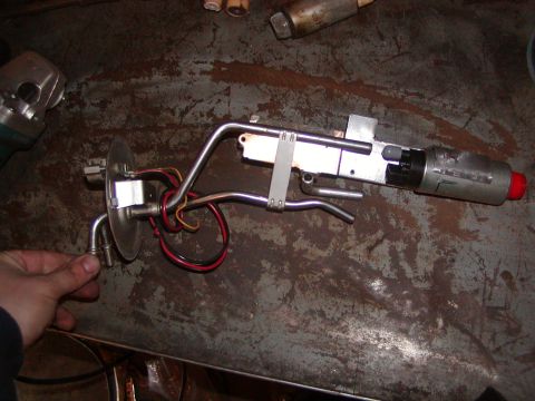 1991 Ford Bronco - A disassembled fuel pump assembly is shown on a metal surface, with a hand holding a metal tube.