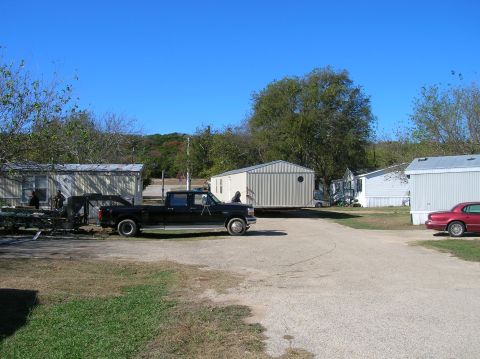 1996 Ford Bronco - A black pickup truck tows a modular building through a residential area with several mobile homes visible.
