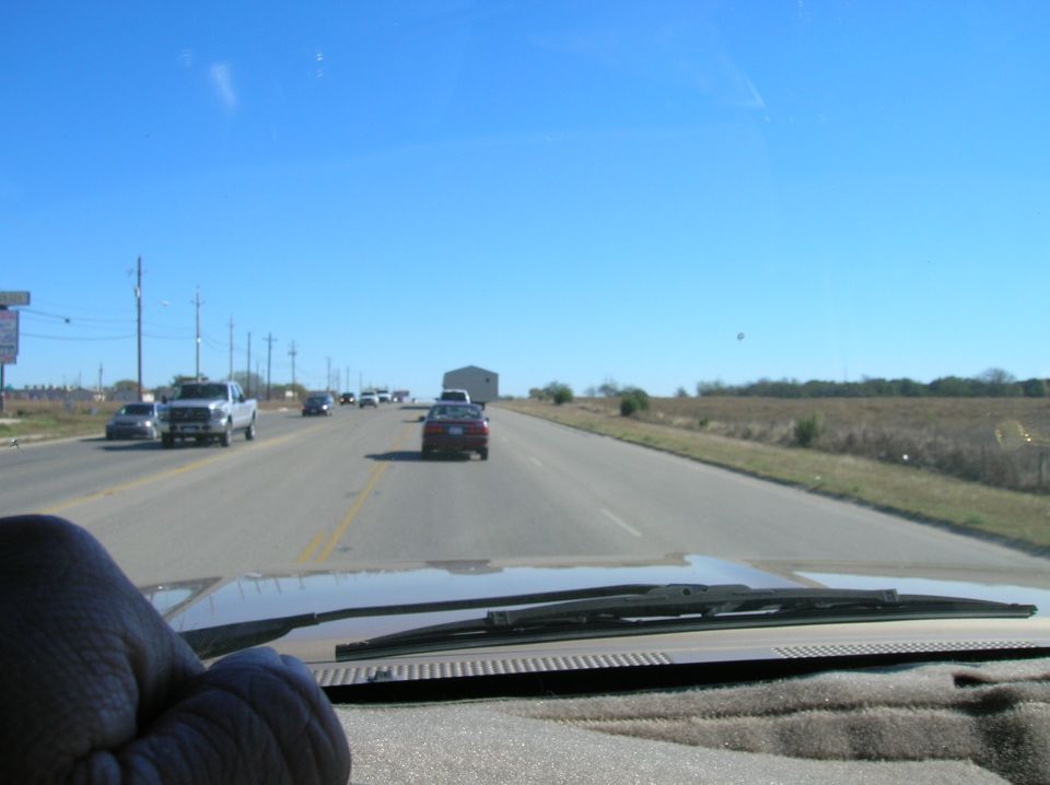 View from inside a vehicle driving on a highway with other cars on the road and a building in the distance