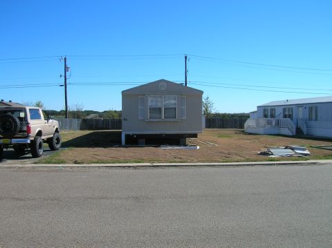 1996 Ford Bronco - A tan Ford Bronco is parked on the side of the road in front of a mobile home under a clear blue sky.