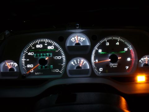 1995 Ford Thunderbird - The illuminated dashboard gauges of a car show the speedometer, tachometer, and fuel levels at night.