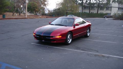 1996 Ford Probe - Red 1996 Ford Probe with black racing stripes parked in a lot.