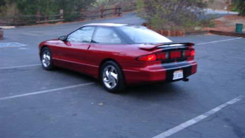 1996 Ford Probe - A red 1996 Ford Probe is parked in a lot, showing its rear end with a spoiler and black stripe detail.