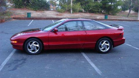 1996 Ford Probe - A red coupe with a spoiler and chrome wheels is parked in a lot.