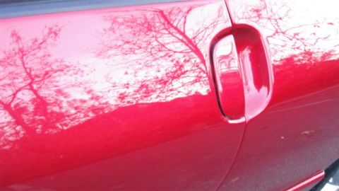1996 Ford Probe - Reflection of bare tree branches is visible on the shiny red paint of a car door.