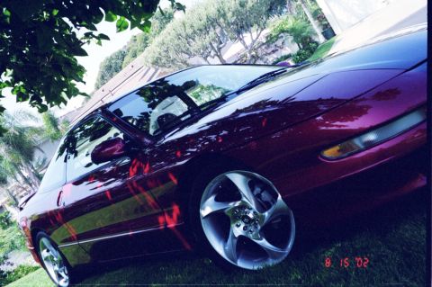 1996 Ford Probe - Dark red 1996 Ford Probe coupe with custom wheels parked outdoors on a grassy lawn.