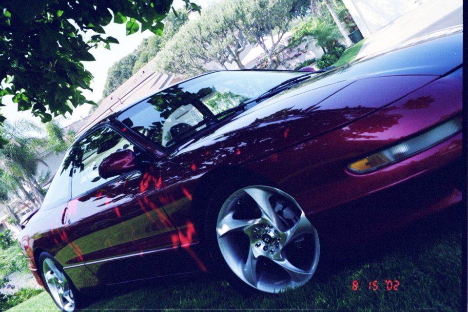 1996 Ford Probe coupe, dark red, parked on grass with trees in background