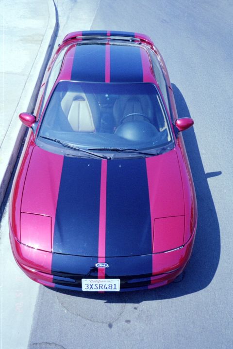 1996 Ford Probe - A red Ford Probe with racing stripes is parked on a street, viewed from above.