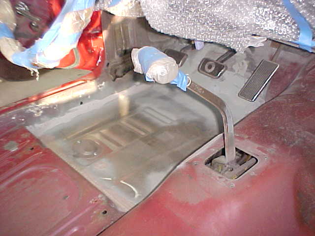 Car interior floor pan with pedals and a gear shifter. Some parts are covered in plastic wrap
