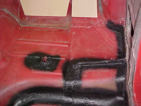 1967 Mercury Cougar - Close-up of a red car's interior floor pan, showing undercoating and taped paper squares.
