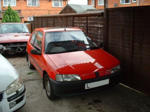 1989 Ford Bronco - A red hatchback is parked in a driveway next to a wooden fence, with other vehicles nearby.